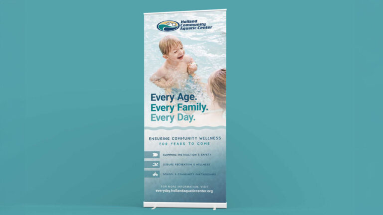 A pull-up banner for the Holland Community Aquatic Center stands against a turquoise background. The banner shows a mother with her child in a pool. The banner reads: "Every age. Every family. Every day. Ensuring community wellness for years to come. Swimming instruction and safety. Leisure recreation and wellness. School and community partnerships. For more information, visit every day dot Holland aquatic center dot org"